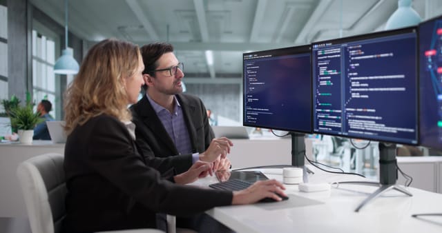 Two people discussing code on a computer screen in an office