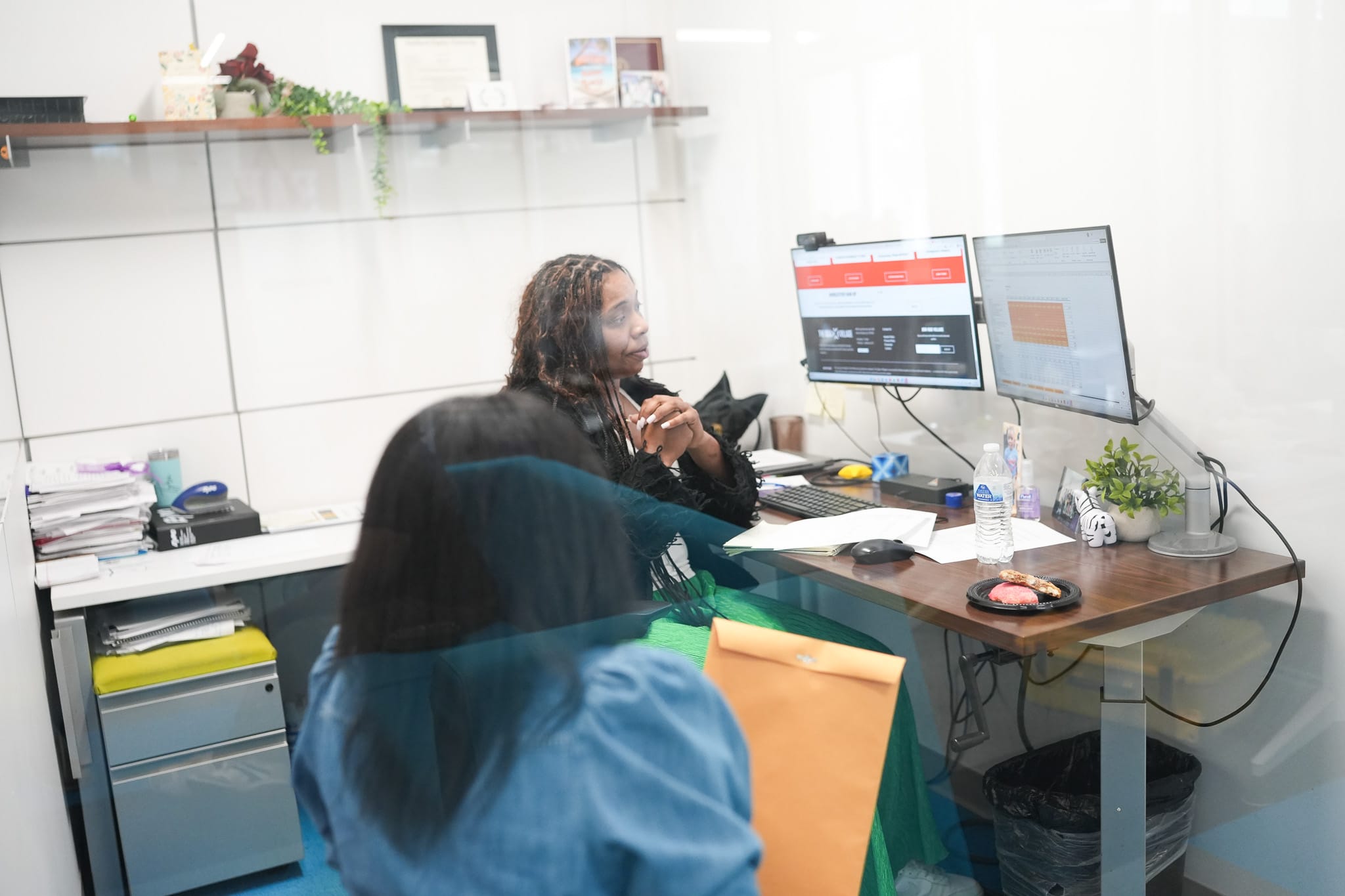 Two women sitting at a desk in an office discussing work.