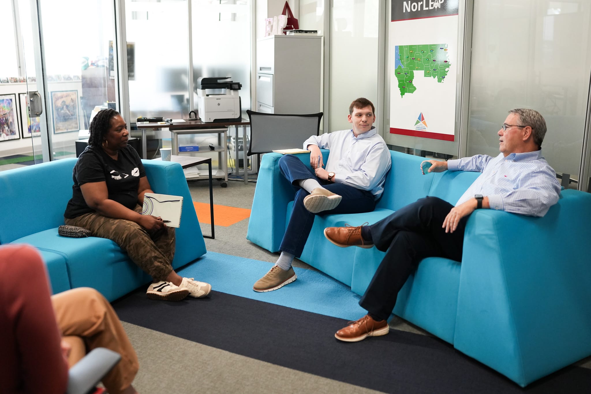 Three people sitting on blue couches having a casual meeting in an office.