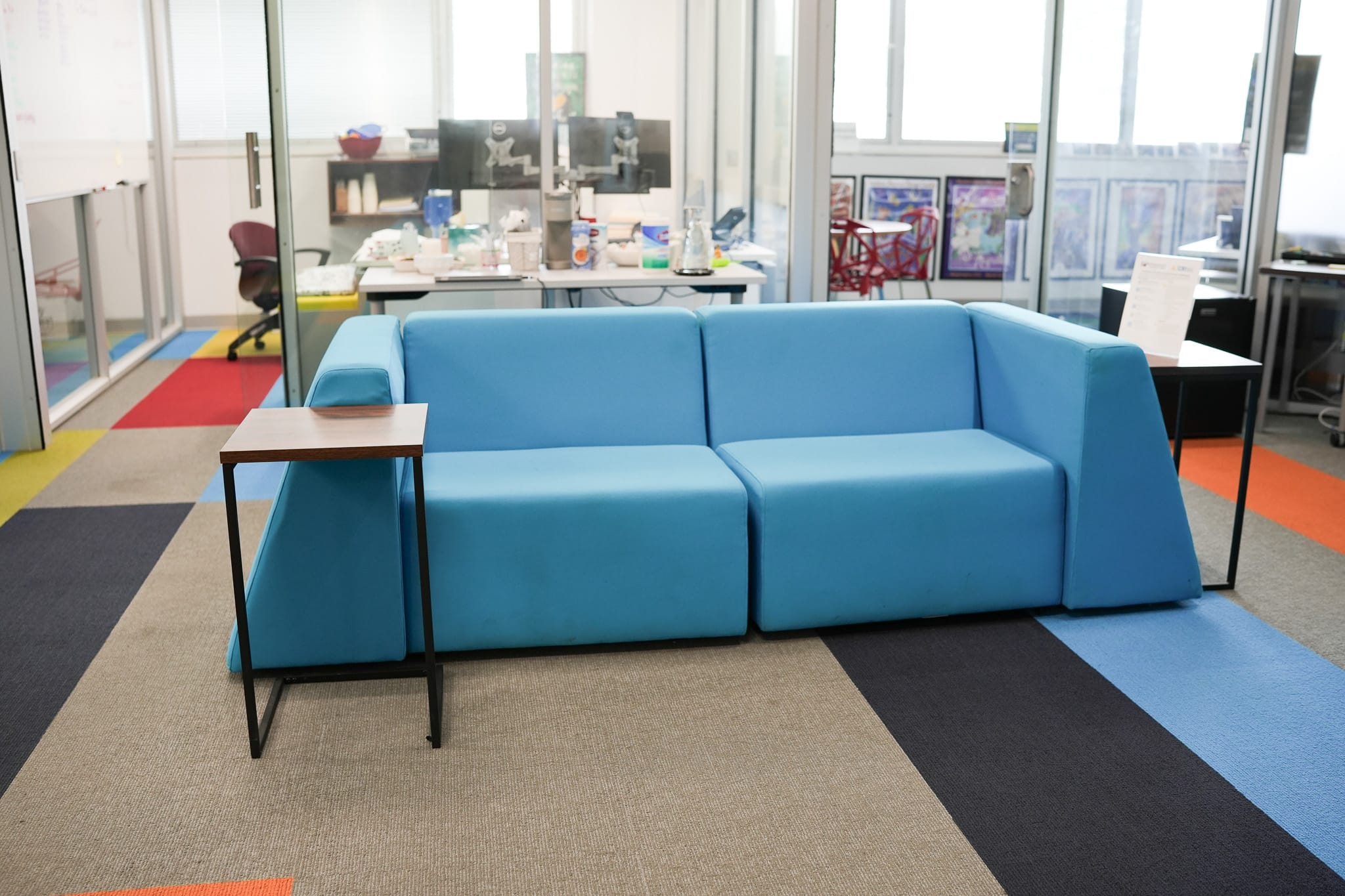 A blue sofa with side tables in an office lounge area with colorful carpet.