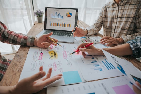 People discussing and pointing at business charts on a wooden table.