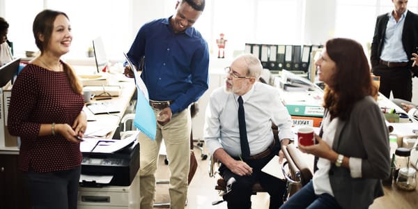 A diverse group of five office workers engaged in conversation and smiling.