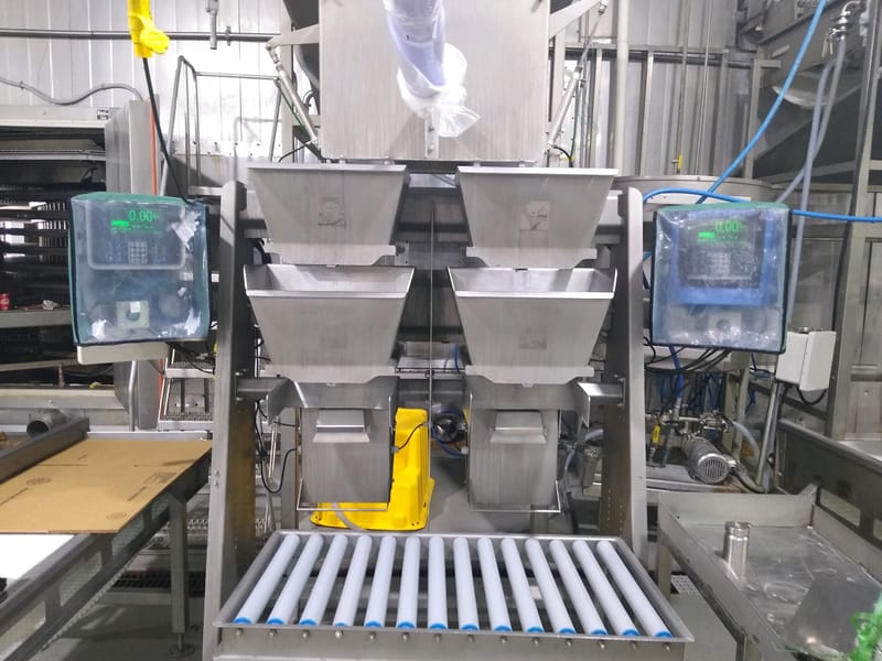 Industrial weighing and filling machine with multiple hoppers and digital displays in a factory setting