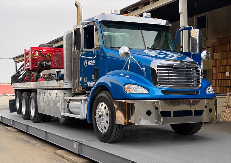 Blue heavy-duty truck on a platform scale being calibrated by Michelli