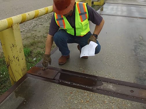 Worker in safety gear inspecting a damaged metal beam during a scale inspection