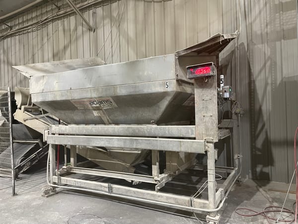 A large metal industrial hopper with a digital display in a warehouse setting.