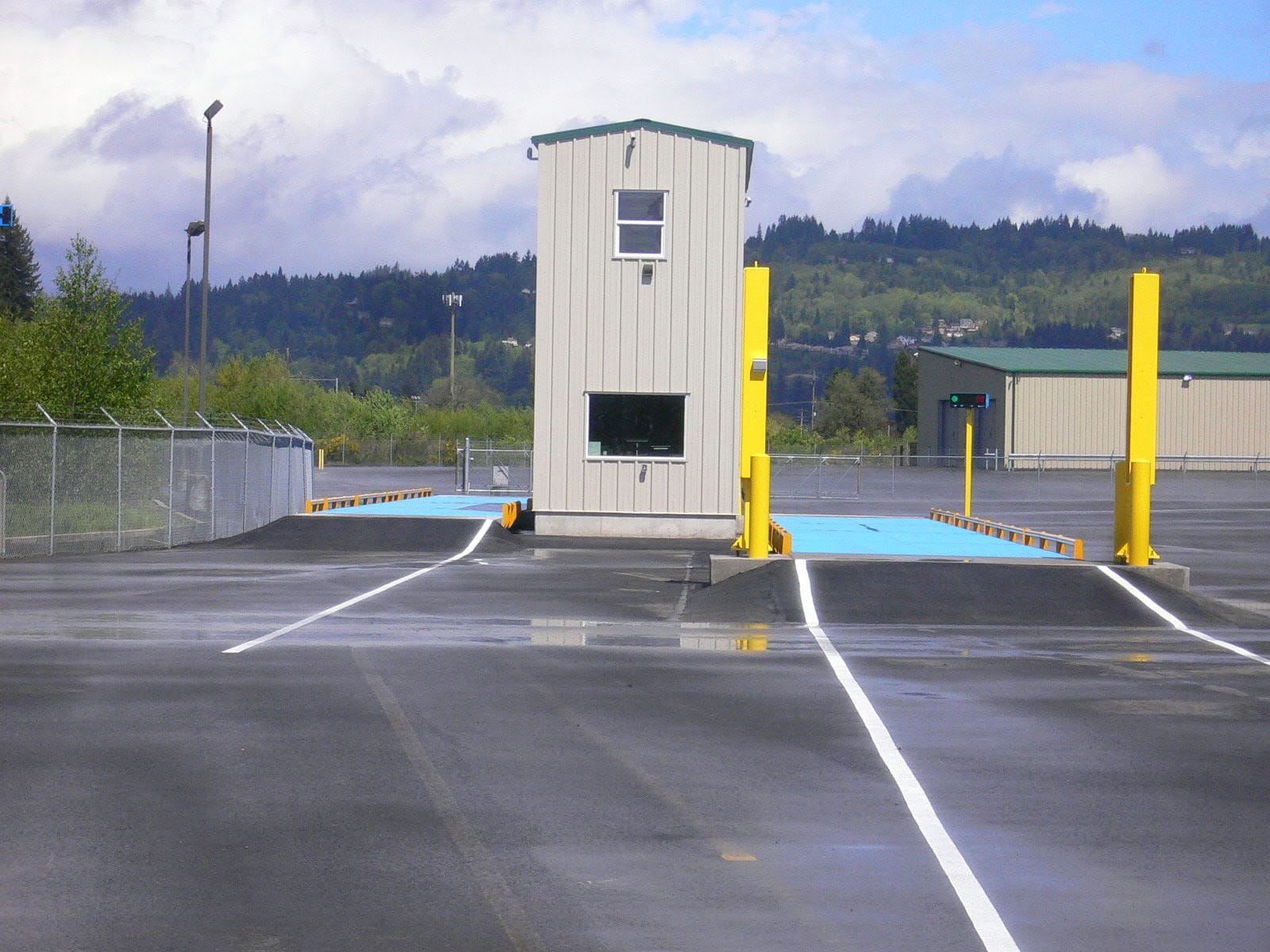 Vehicle inspection station with scale house between two yellow columns on a ramp for aggregate truck weighing and loadout