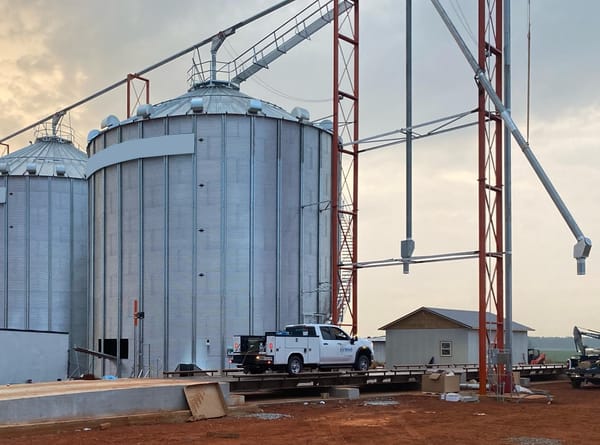 Utility truck parked in front of large grain silos at an industrial agriculture site