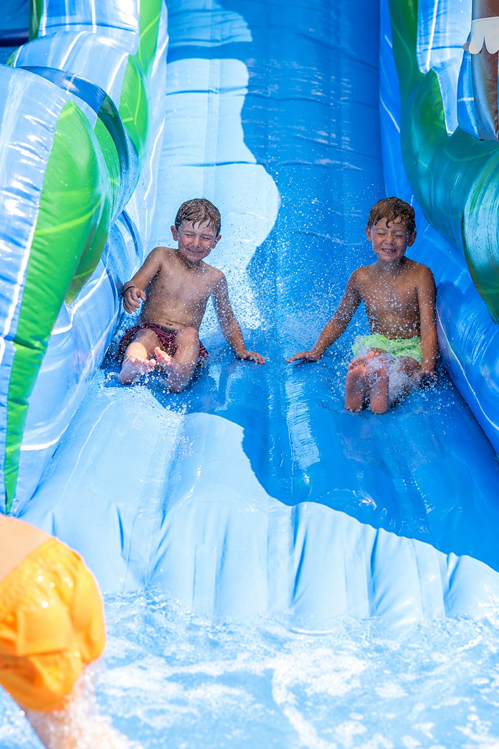 Two young boys sliding down a colorful inflatable water slide.
