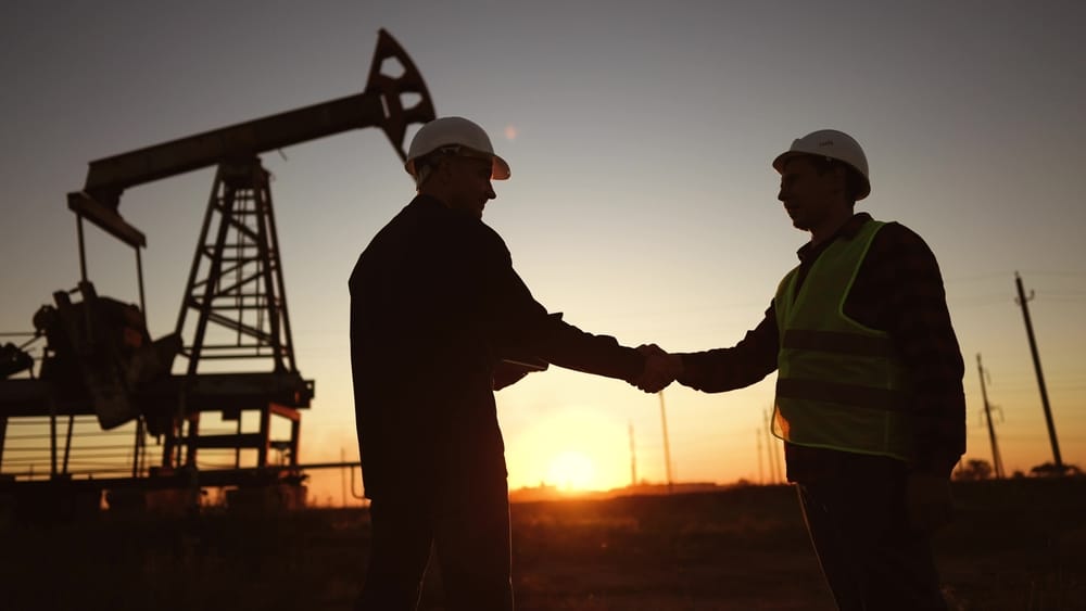 Two energy professionals shaking hands at an oil field at sunset