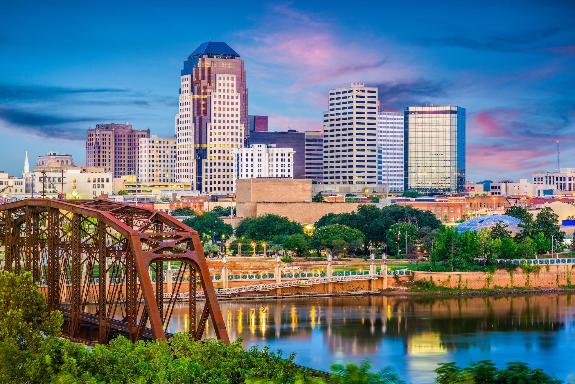 Downtown Shreveport skyline with a bridge and river in the foreground at dusk.