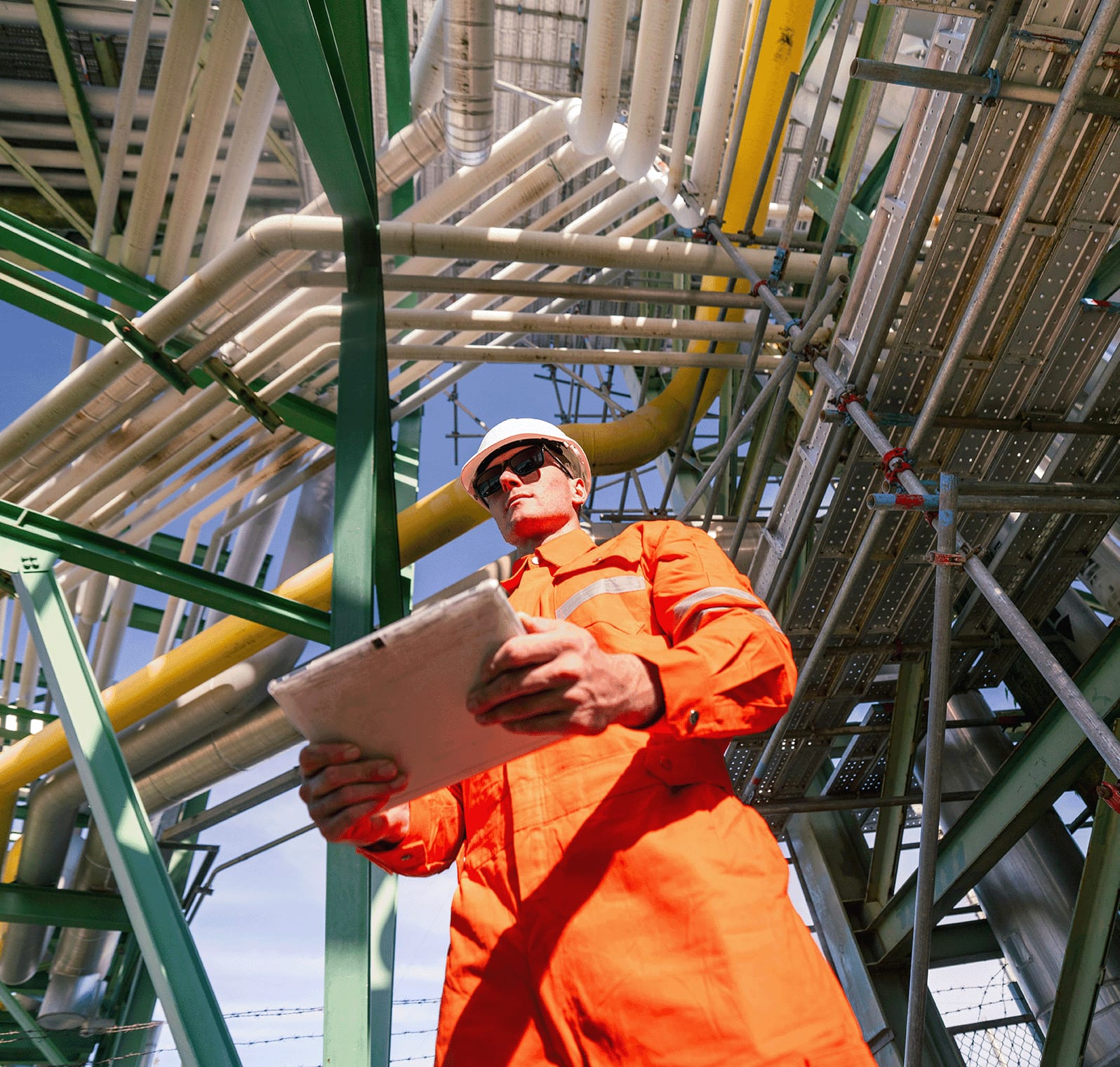 Worker in safety gear under process piping at an industrial plant